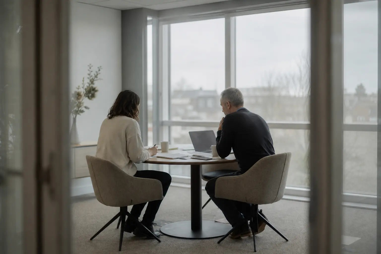 Deux personnes de part et d’autre d’une petite table de réunion, documents et ordinateur portable entre elles