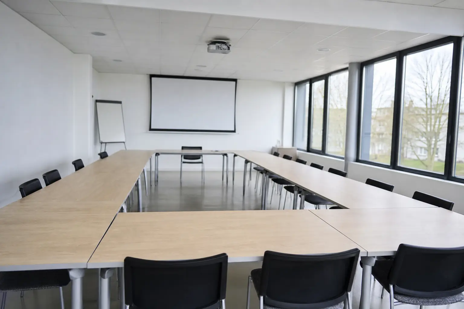 Salle de formation vide et lumineuse, tables disposées en U devant un écran de projection éteint