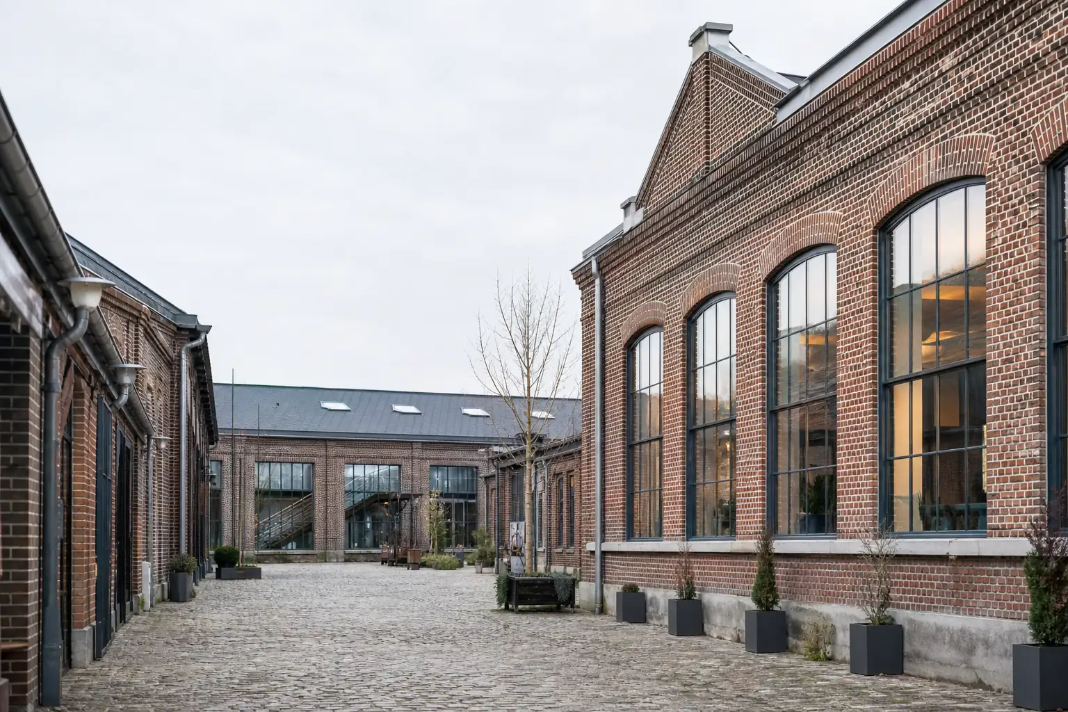 Anciens bâtiments industriels en brique reconvertis en bureaux, grandes verrières d’atelier sur cour pavée